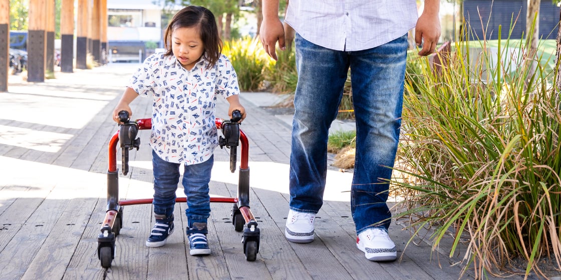 Young latino boy with down syndrome walks using a walker next to his father