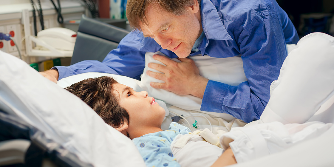 Father speaking to his son as the son lies in a hospital bed