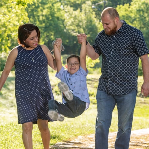 Parents swing their young boy in the park.