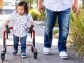 Young latino boy with down syndrome walks using a walker next to his father