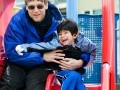 Father and young son on a playground slide. Son has cerebral palsy.